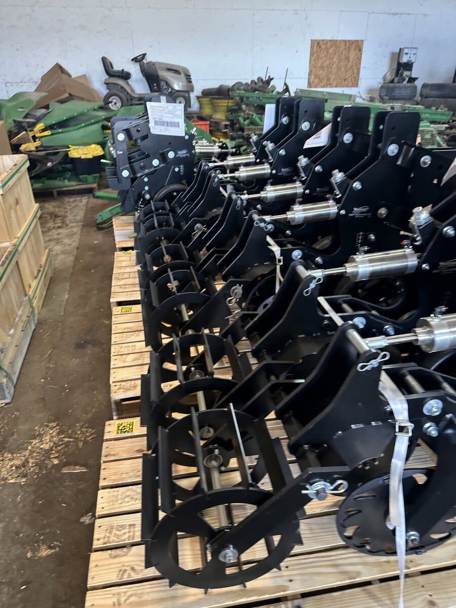 Row of new black planter closing wheel attachments staged on pallets in a warehouse