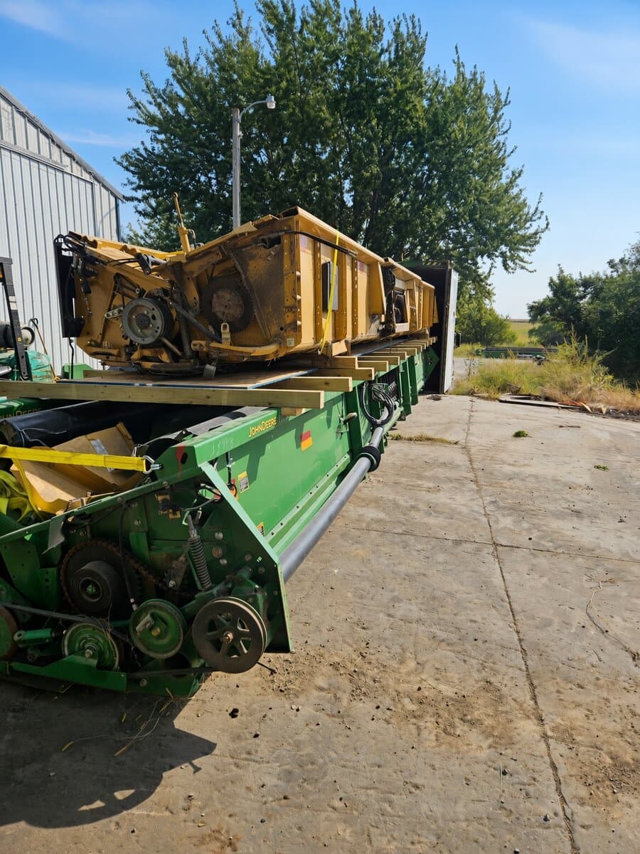 A header stacked on wooden dunnage atop a green John Deere header, staged outdoors
