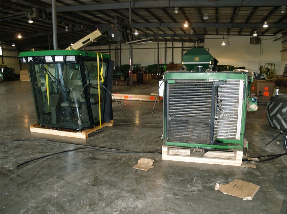Cabine de operador John Deere e um módulo de radiador presos a patins de embarque em um armazém