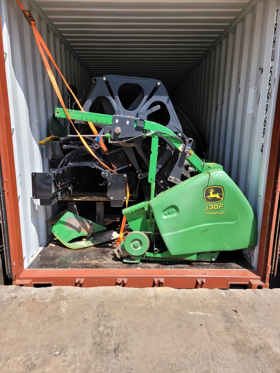 Green John Deere 630F HydraFlex header strapped upright inside a shipping container