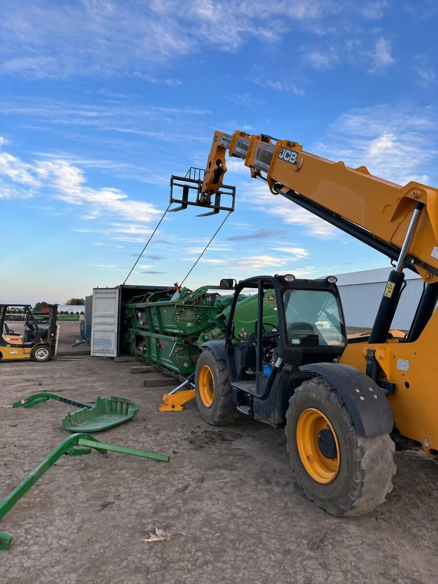 Manipulador telescópico JCB amarelo ao lado de uma plataforma verde John Deere carregada em um contêiner aberto