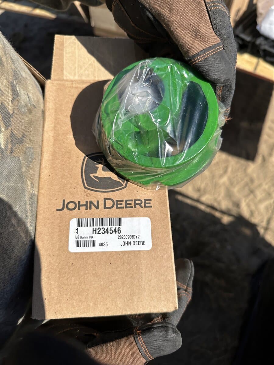 Gloved hand holding a wrapped John Deere part on its branded parts box
