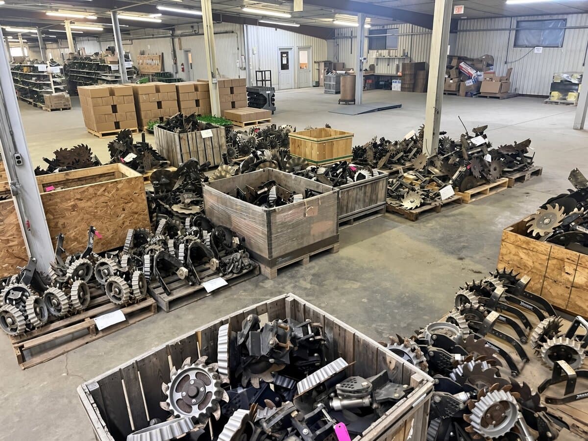 Wooden crates and pallets of John Deere disc blades, closing wheels and row-unit parts on a warehouse floor