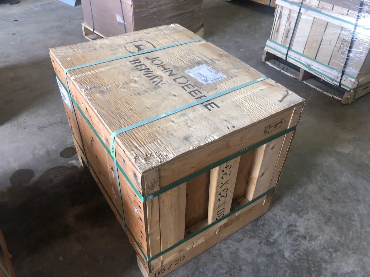Wooden shipping crate stenciled John Deere Reman with dimensions marked, on a warehouse floor